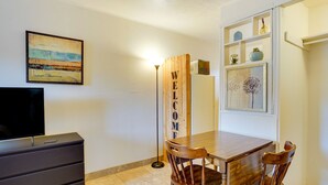 A room with a wooden dining table, two wooden chairs, a TV on a cabinet, a painting on the wall, and a 'WELCOME' sign. - Budget-friendly Tucson Studio: 2 Mi to University! (Tucson)