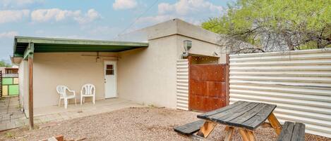 Un patio con una mesa y sillas de madera, un muro de metal corrugado y una puerta que da a un porche cubierto.