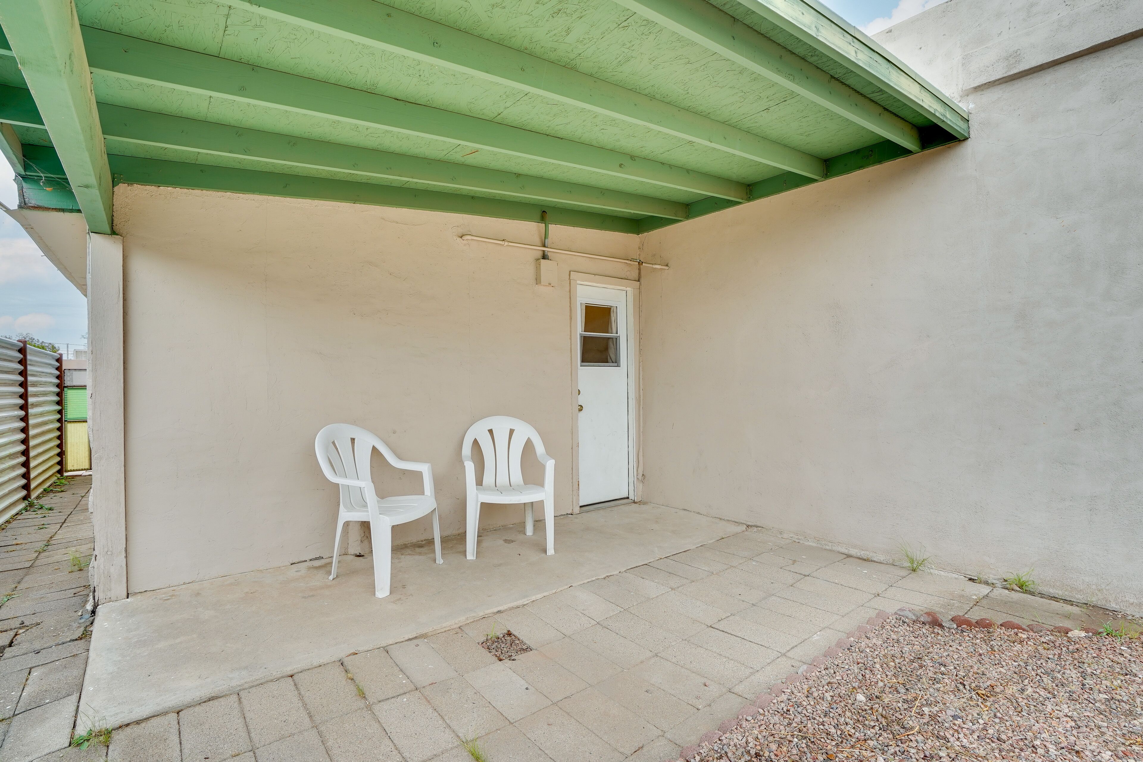 A covered patio area with two white plastic chairs, a door, and a concrete floor.