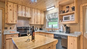 Una cocina con armarios de madera, encimera de granito, una botella de vino y lavavajillas.