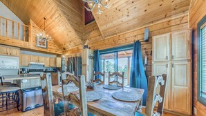 A wooden cabin with a dining area, kitchen, and large windows.