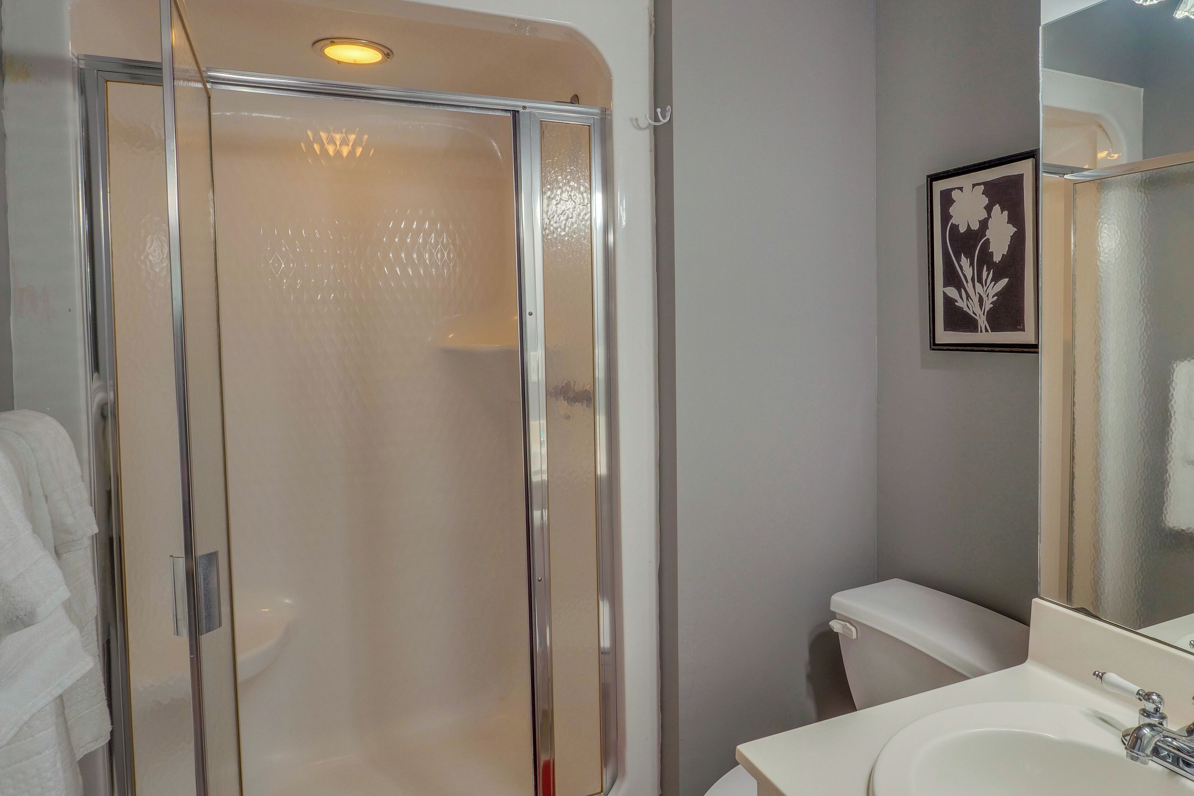 Un baño con ducha de mampara de vidrio, inodoro blanco y lavamanos con espejo.