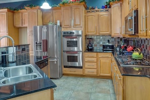 A kitchen with wooden cabinets, stainless steel appliances, a double sink, and a tiled backsplash.