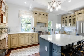 A spacious kitchen with cream-colored cabinets, a large island, a stainless steel refrigerator, and a chandelier. - Private Hot Tub: Historic Savannah Home (Savannah)