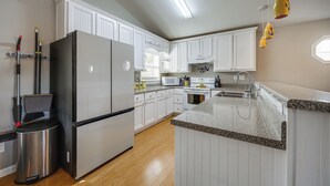 A modern kitchen with white cabinetry, a stainless steel refrigerator, a microwave, and a granite countertop. - Lakefront Eatonton Getaway w/ Dock & Grill! (Eatonton)