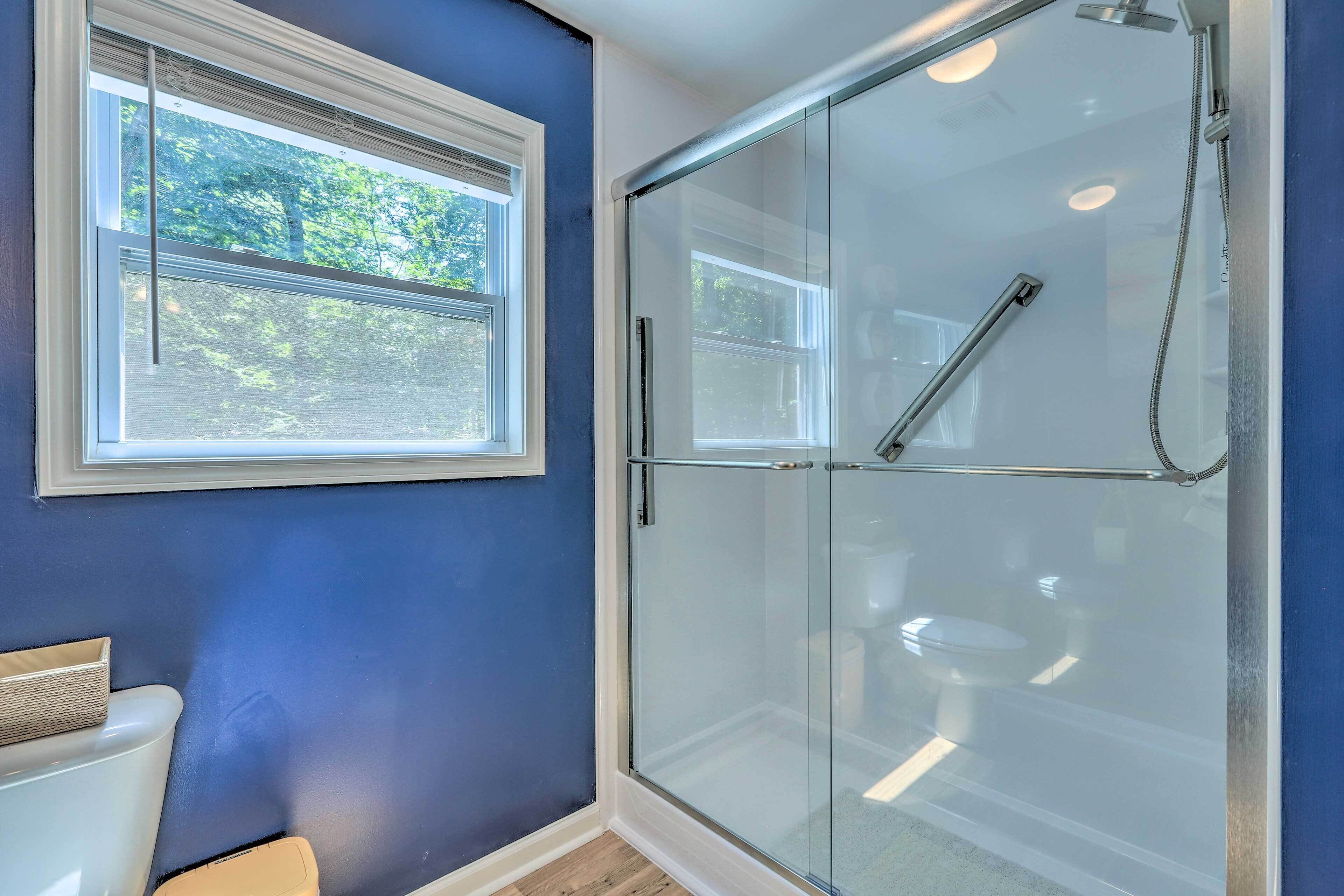 A bathroom with a glass shower enclosure, a white toilet, and a window with a view of trees.