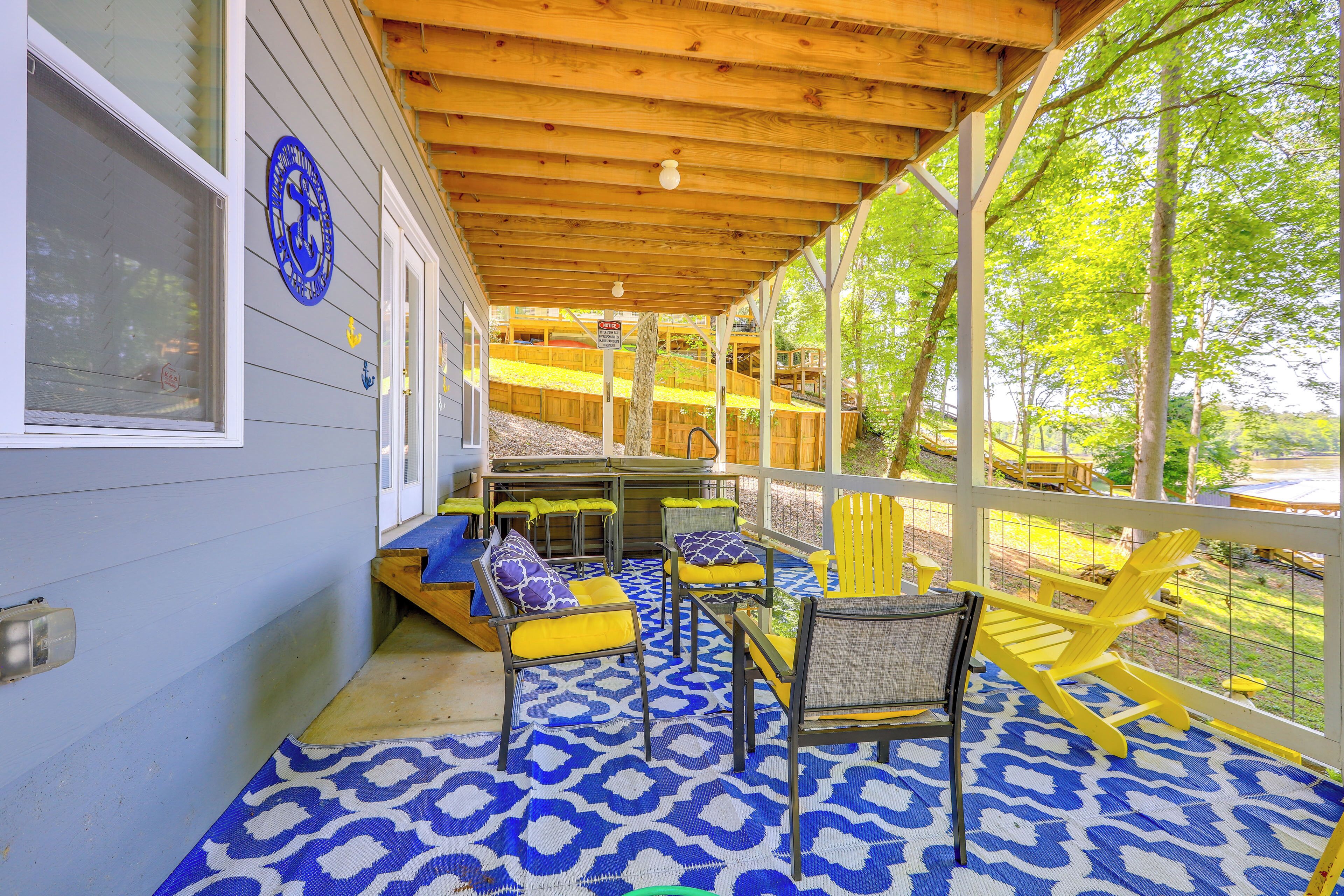 Een overdekt terras met blauw patroon op de vloer, gele en grijze stoelen en een houten plafond.
