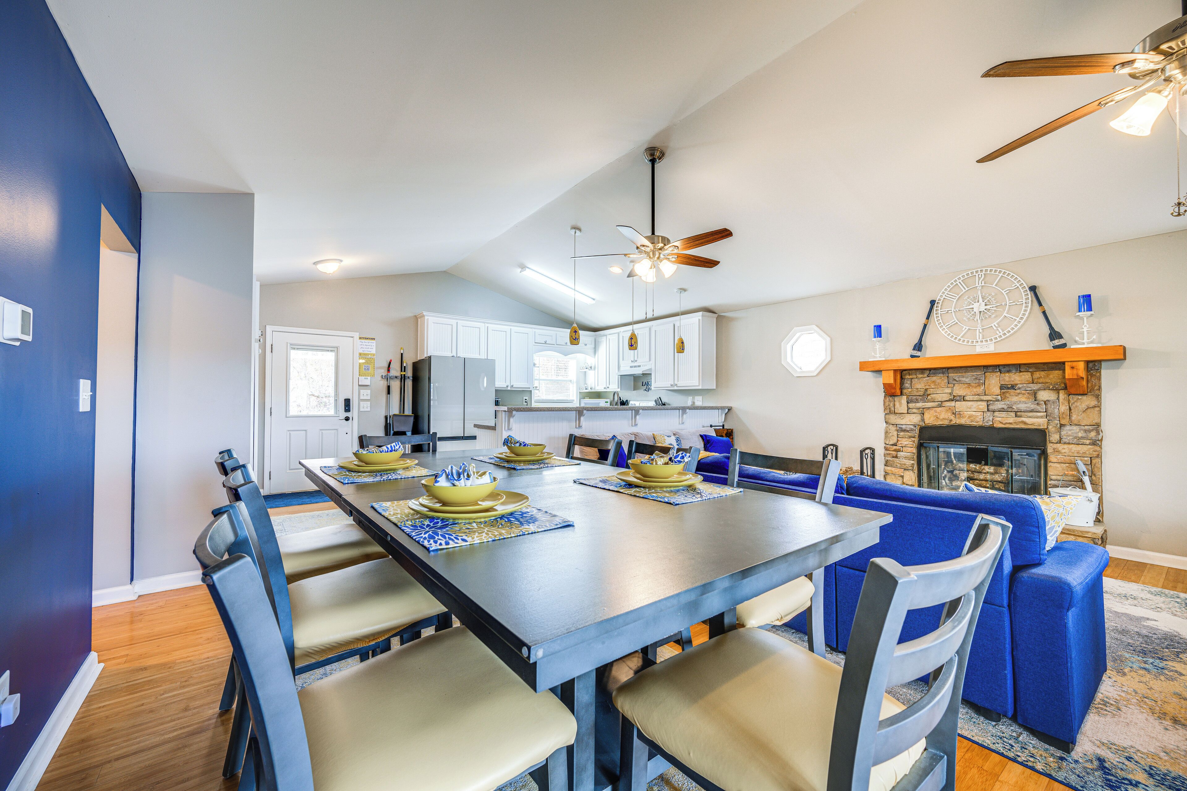 Une cuisine moderne avec des meubles blancs, une table à manger dressée pour six personnes et un canapé bleu dans l’espace salon.