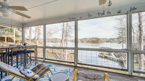 A sunroom with large windows overlooking a lake, wicker furniture, and a ceiling fan. - Lakefront Eatonton Getaway w/ Dock & Grill! (Eatonton)