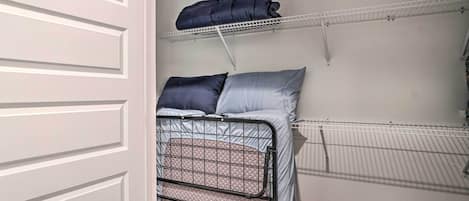 A compact room with a bed, a shelf above it, and a door.