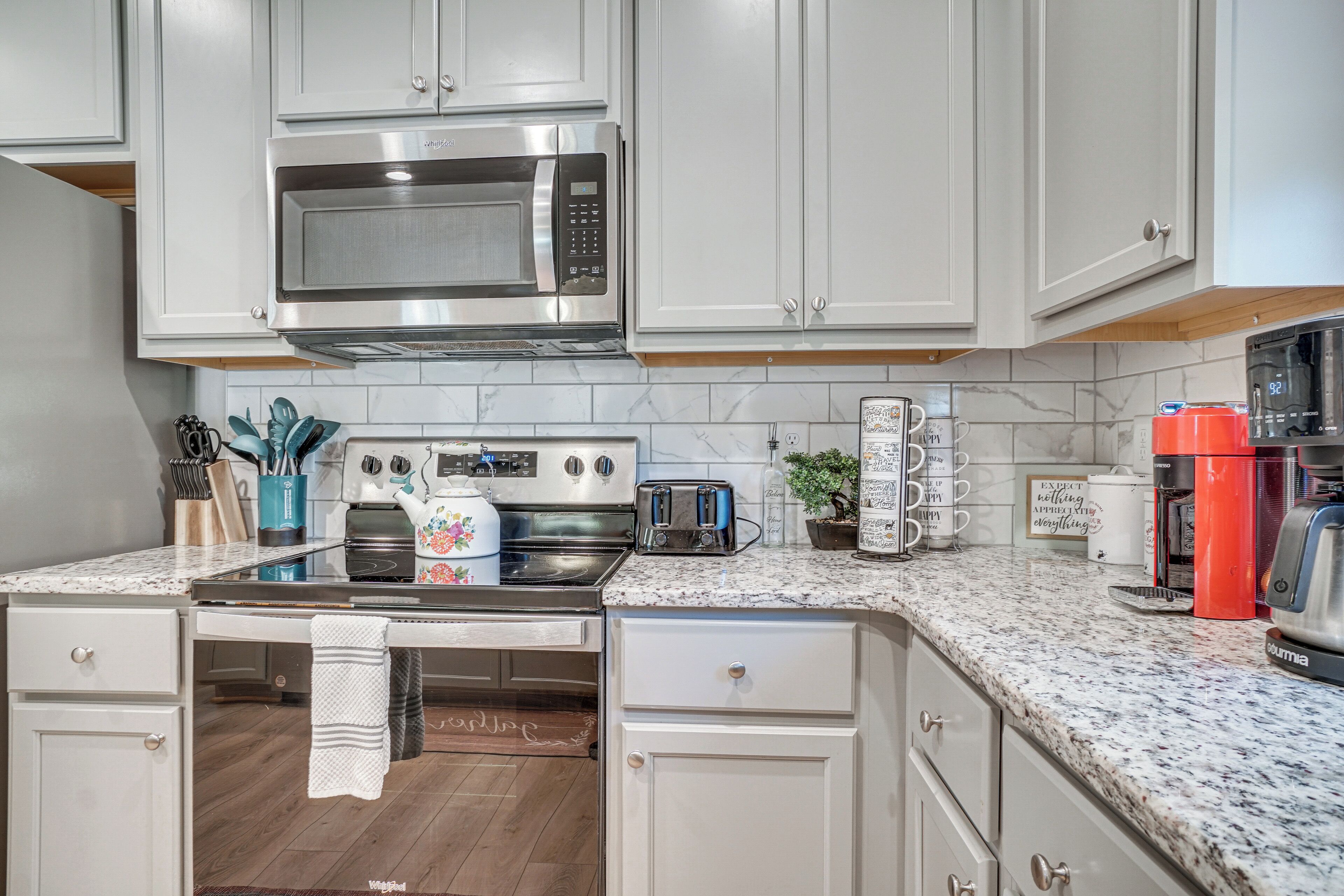 A modern kitchen with white cabinets, stainless steel appliances, a granite countertop, and a coffee maker.