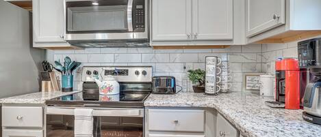 Una cocina moderna con armarios blancos, electrodomésticos de acero inoxidable, encimera de granito y cafetera.