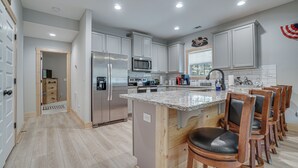 Een moderne keuken met witte kasten, roestvrijstalen apparatuur en een centraal eiland met barkrukken.