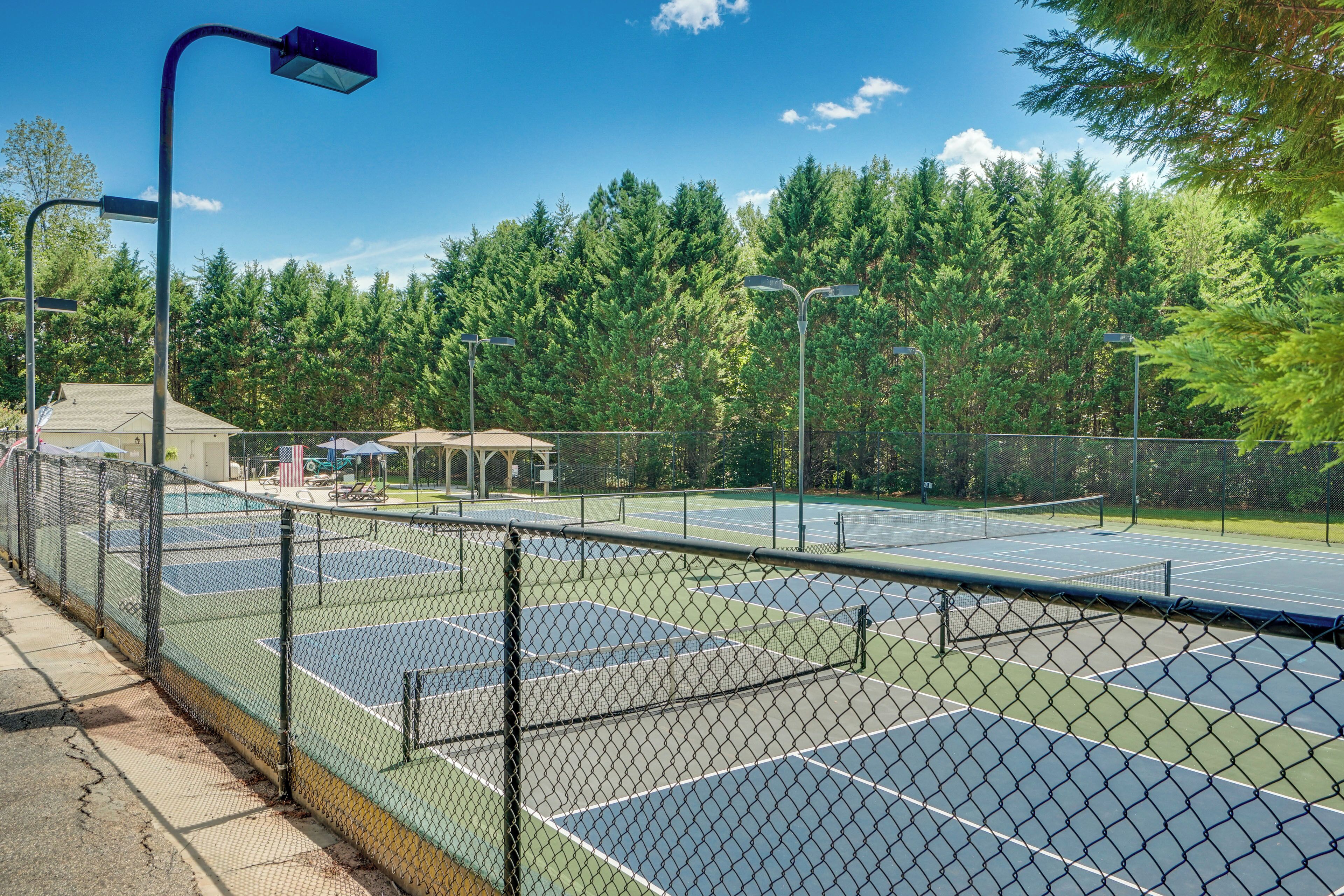 En tennisbana med ett stängsel av sammanlänkade kedjor, omgiven av träd och en lusthus.
