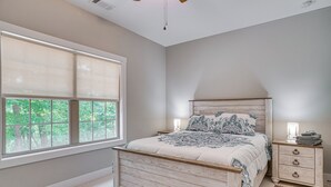 Een slaapkamer met een houten bed, nachtkastje, lamp en een raam met jaloezieën.