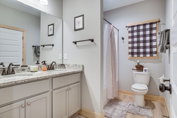 A bathroom with a marble countertop, a toilet, a shower curtain, and a towel rack. - Luxury Helen Retreat Hot Tub & Game Room (Helen)