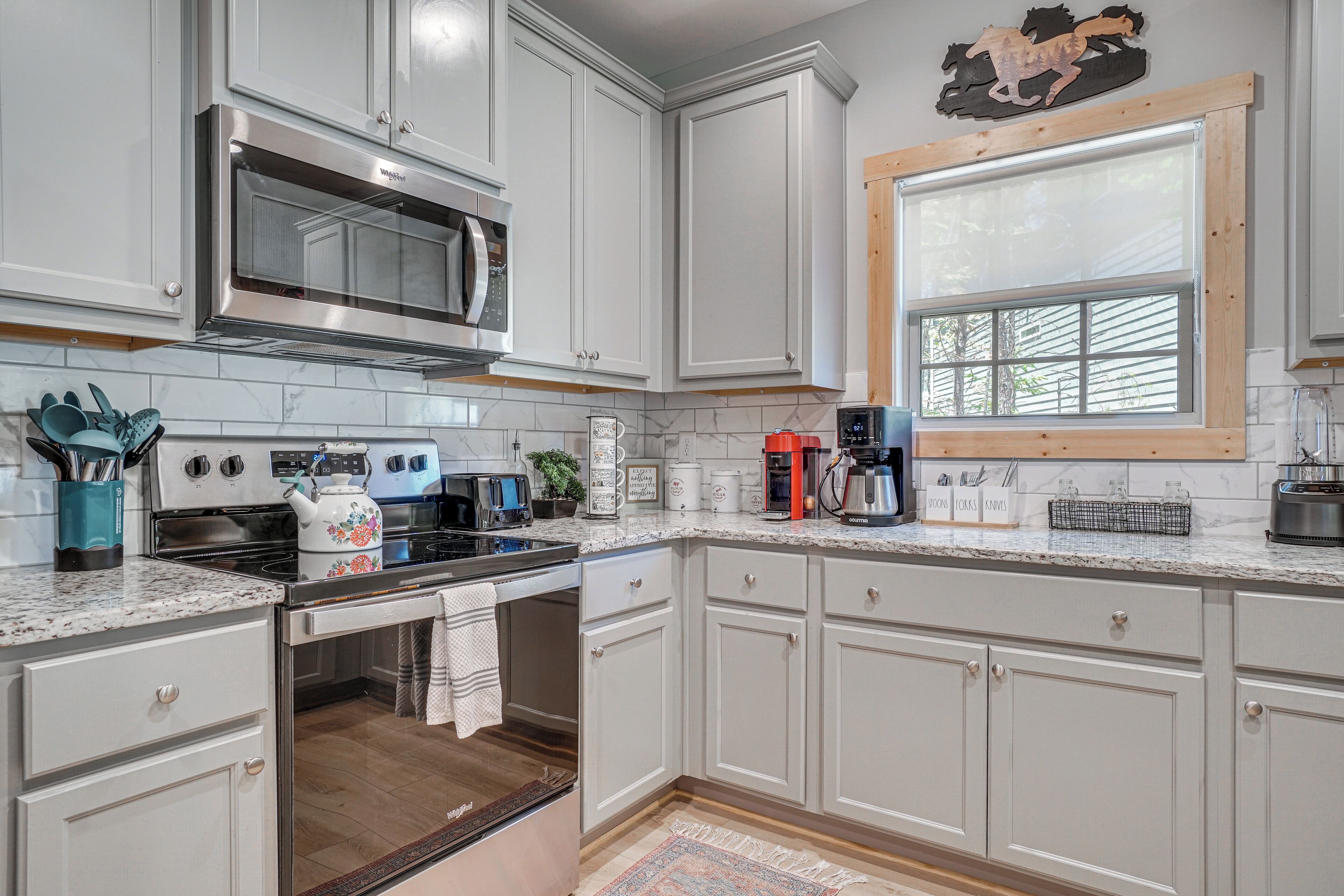 A kitchen with white cabinets, a microwave, a stove, and a window with blinds.