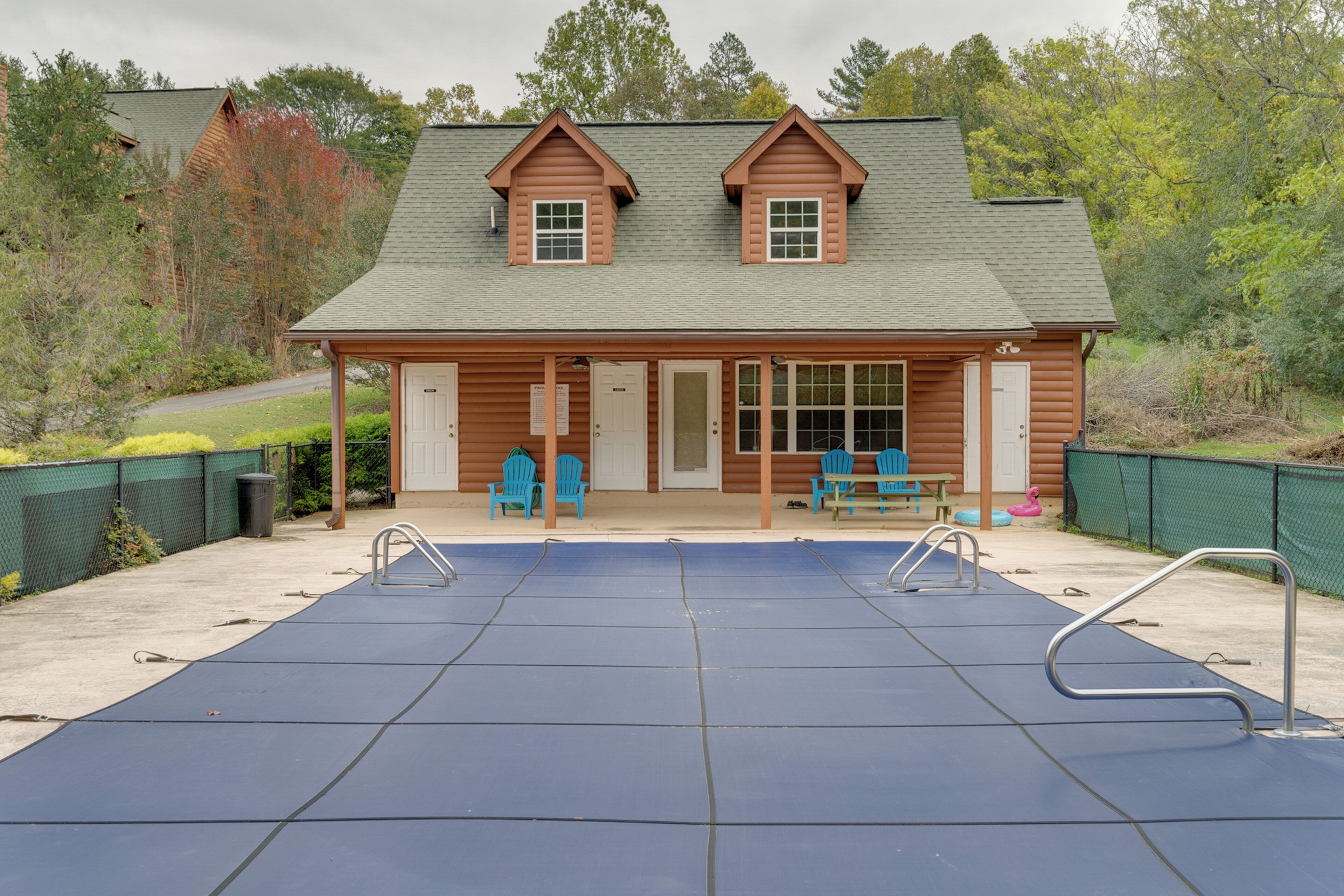 A log cabin with a swimming pool, two porches with chairs, and a fenced yard.