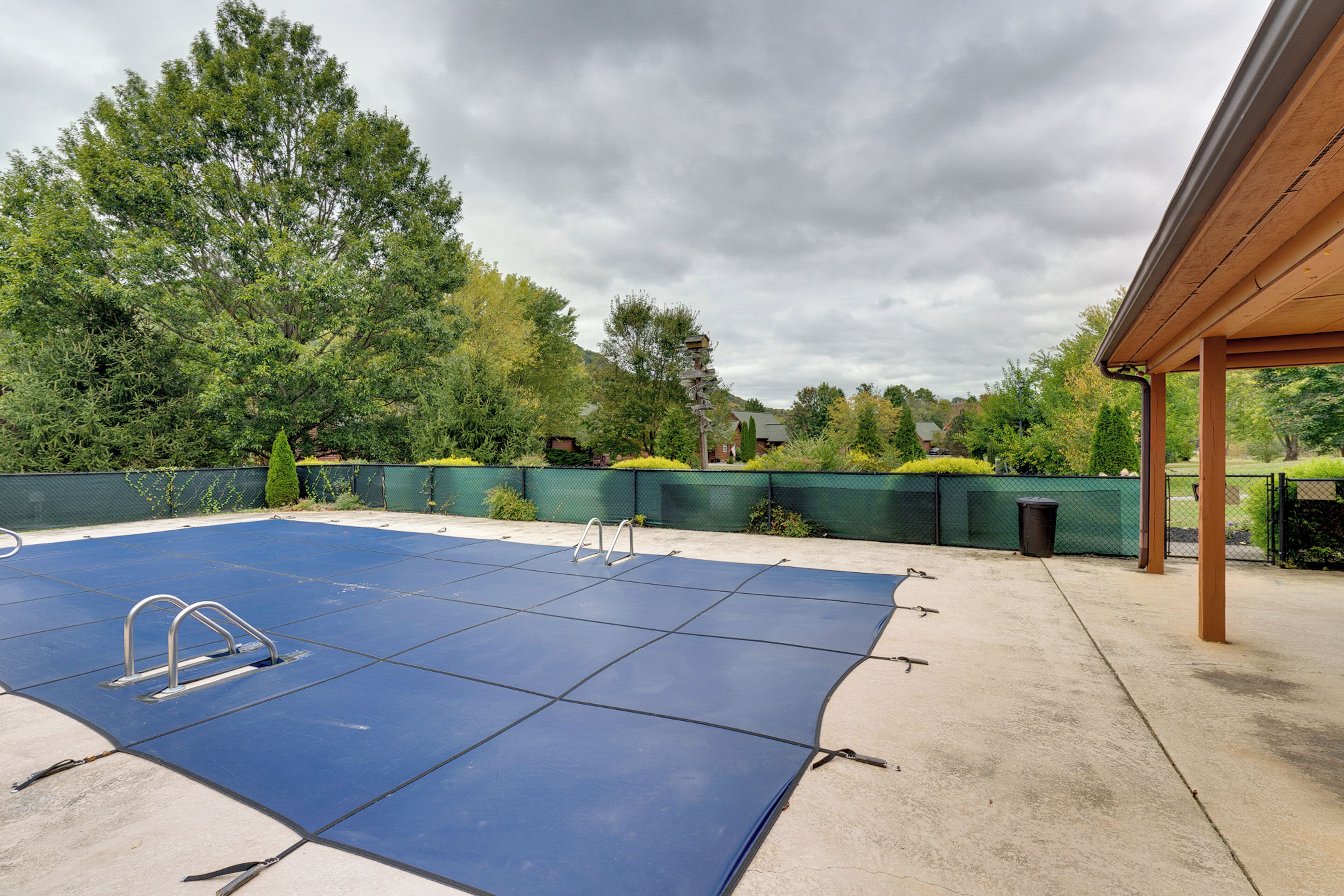 Ein Swimmingpool mit Sprungbrett, umgeben von einem grünen Zaun und Bäumen.