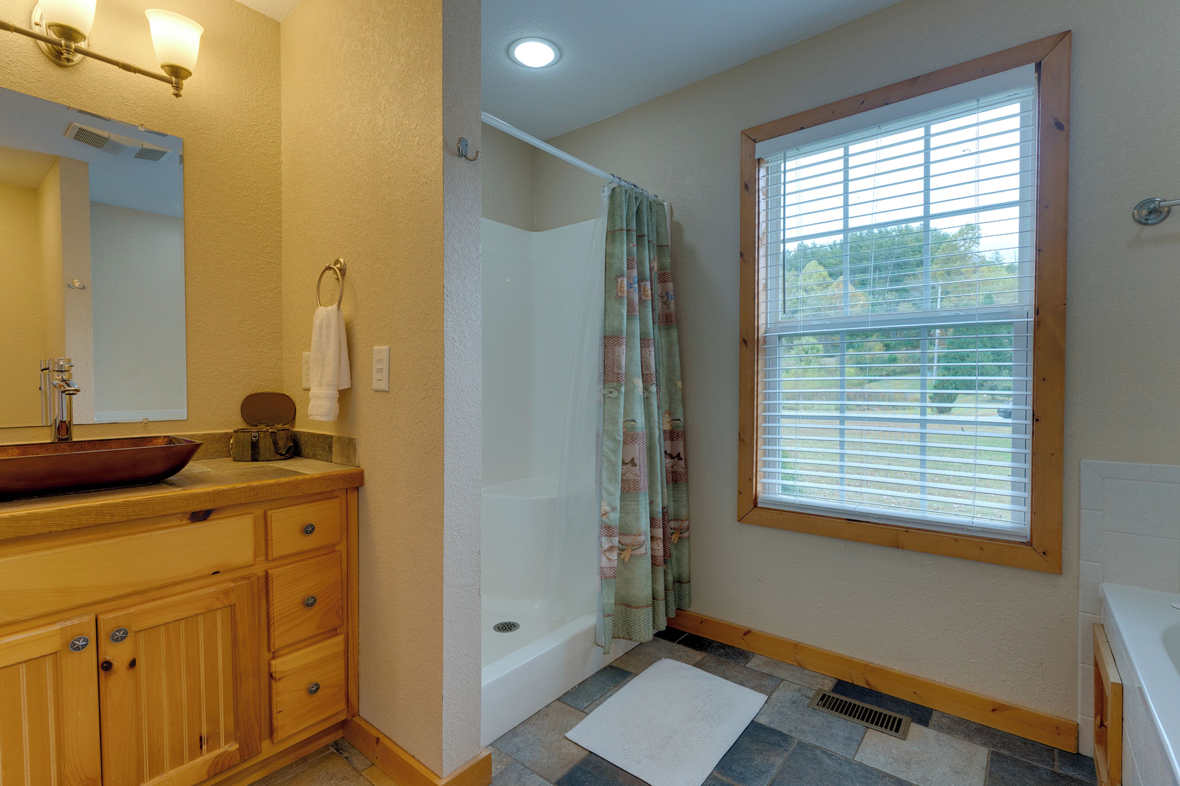 A bathroom with a wooden vanity, a bathtub, a shower curtain, and a window with blinds.