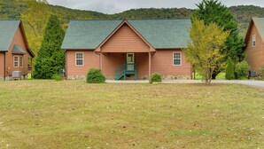 A log cabin with a green staircase, surrounded by a grassy area and trees.