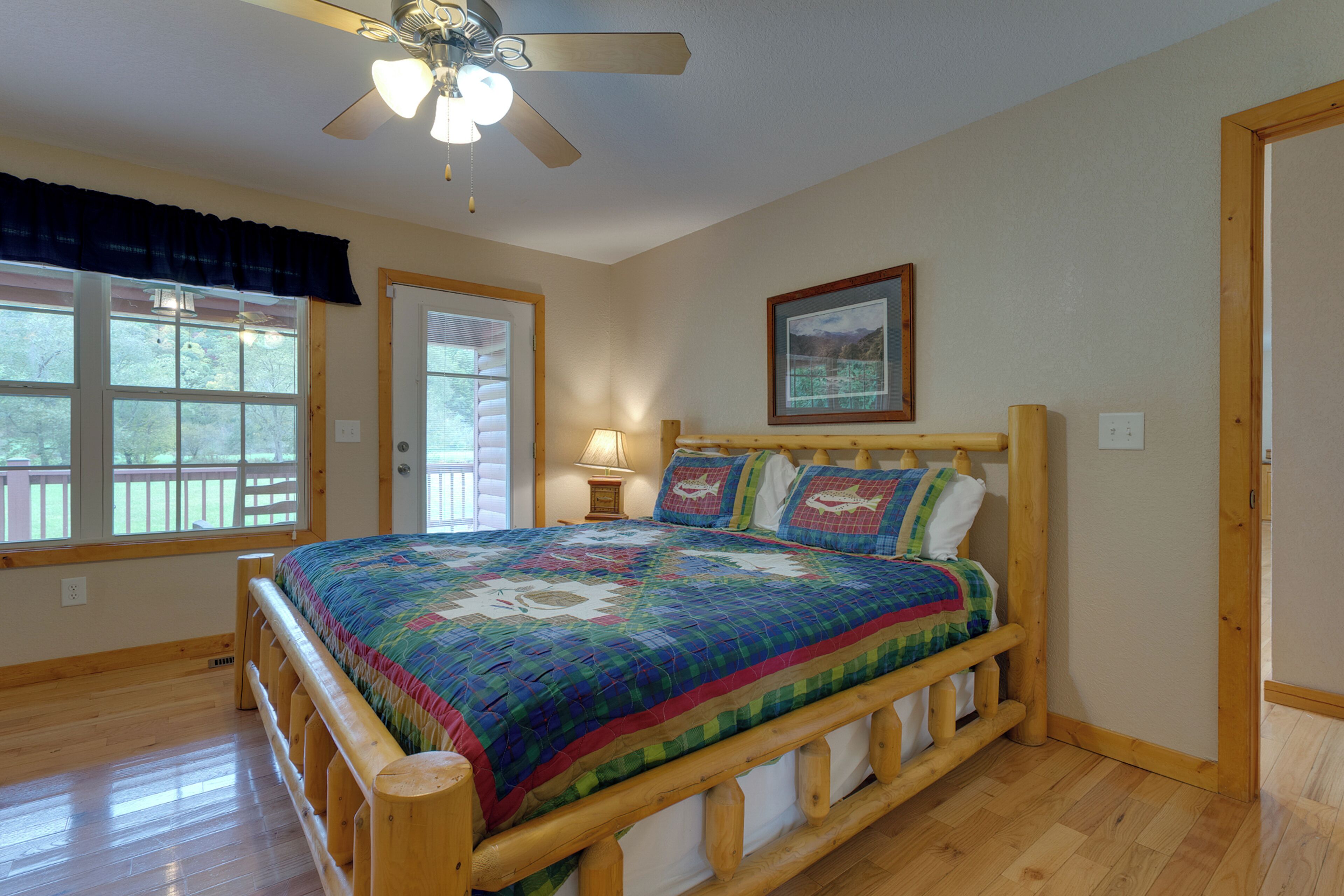 A bedroom with a wooden bed frame, a quilt, a ceiling fan, and a window with a view of the outdoors.