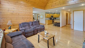 A spacious living area with a wooden ceiling, a sofa, a coffee table, and a kitchen in the background.