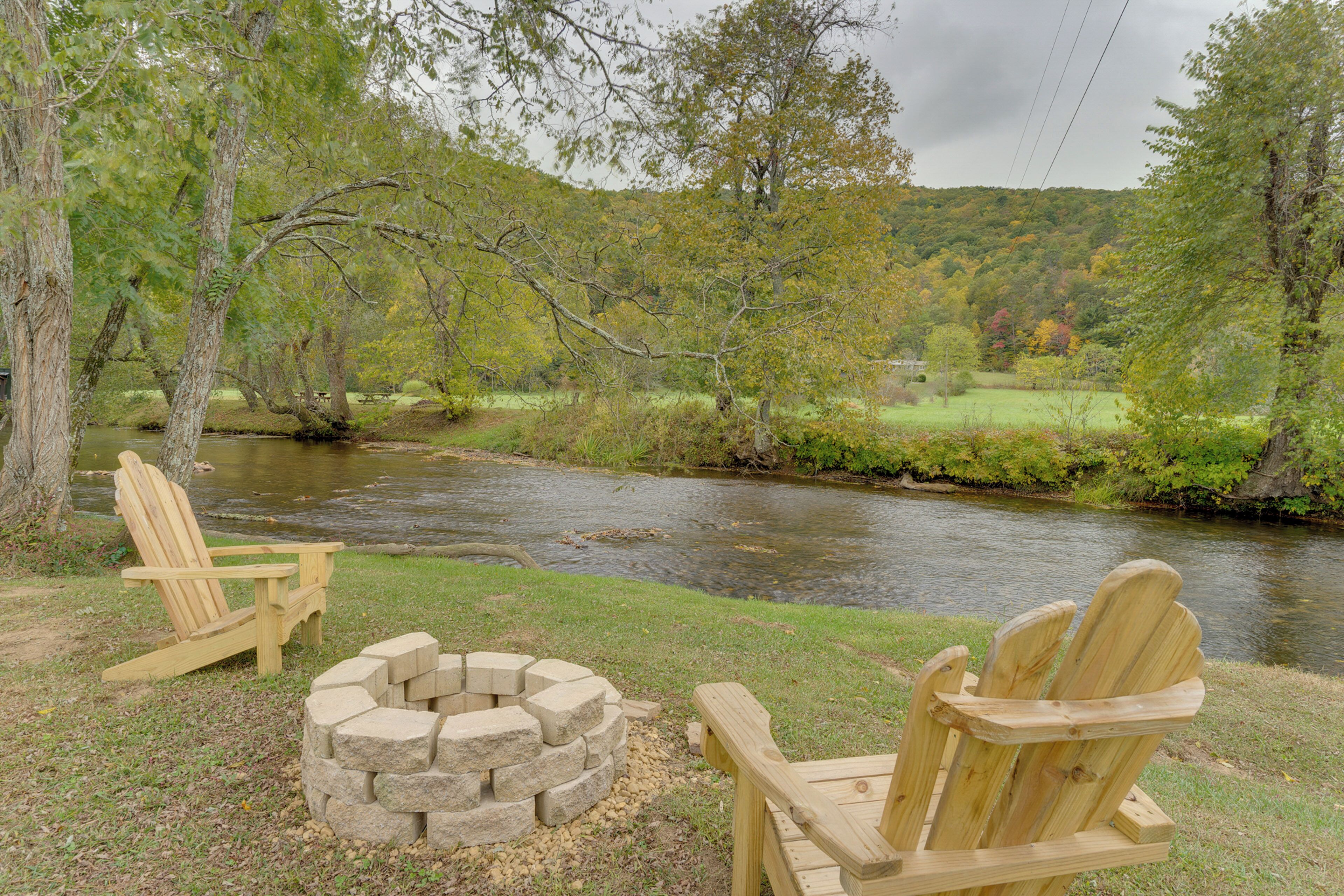 A riverside campsite with two wooden Adirondack chairs and a stone fire pit.