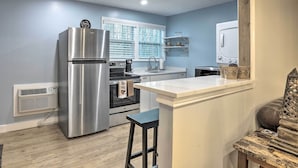 A modern kitchen with a stainless steel refrigerator, oven, and microwave. There is a window with blinds, a white countertop, and a small island with stools. - Atlanta Area Studio ~ 3 Mi to Gas South Arena! (Lawrenceville)