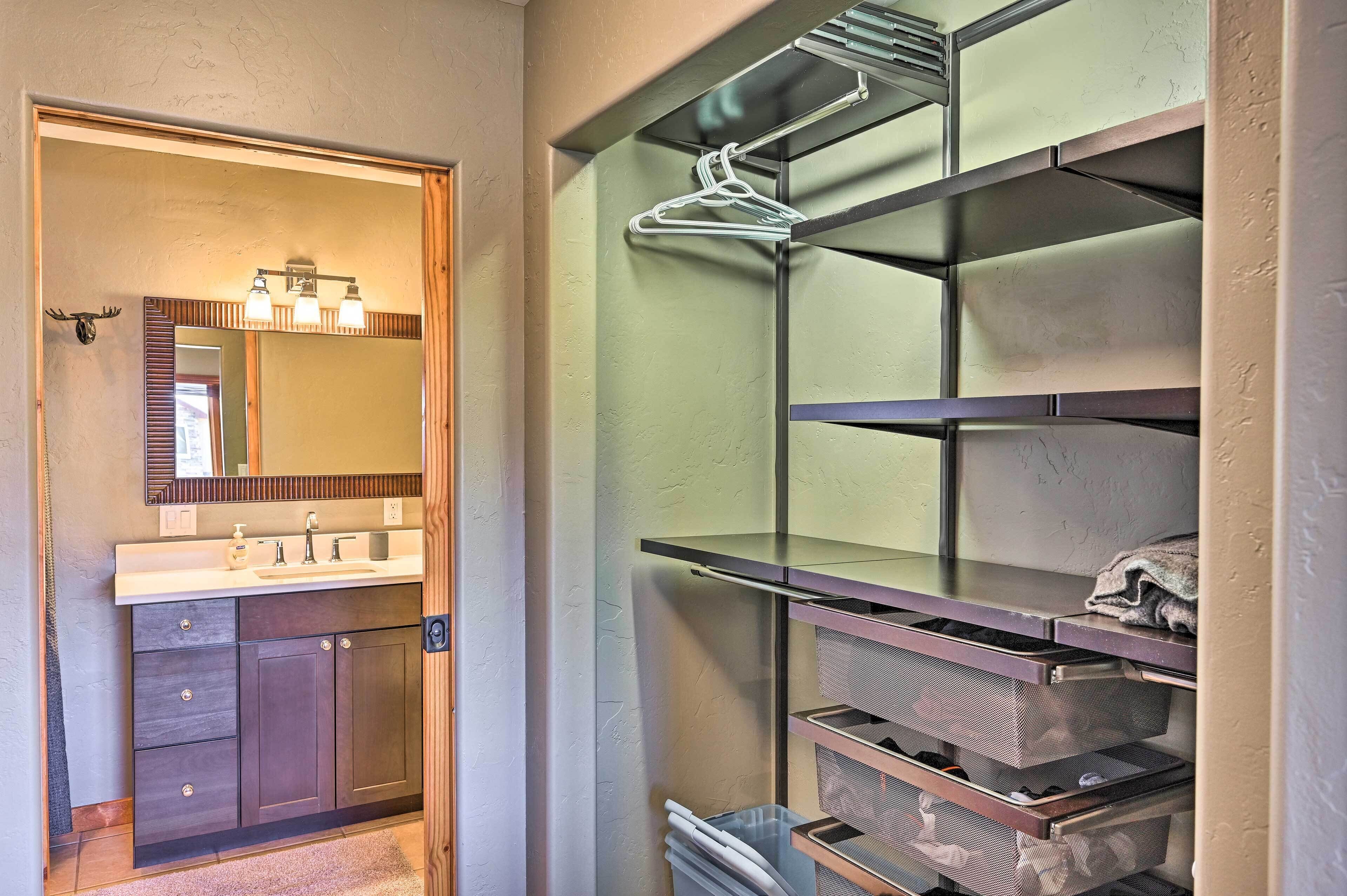 A bathroom with a vanity, mirror, and shelves with storage bins.