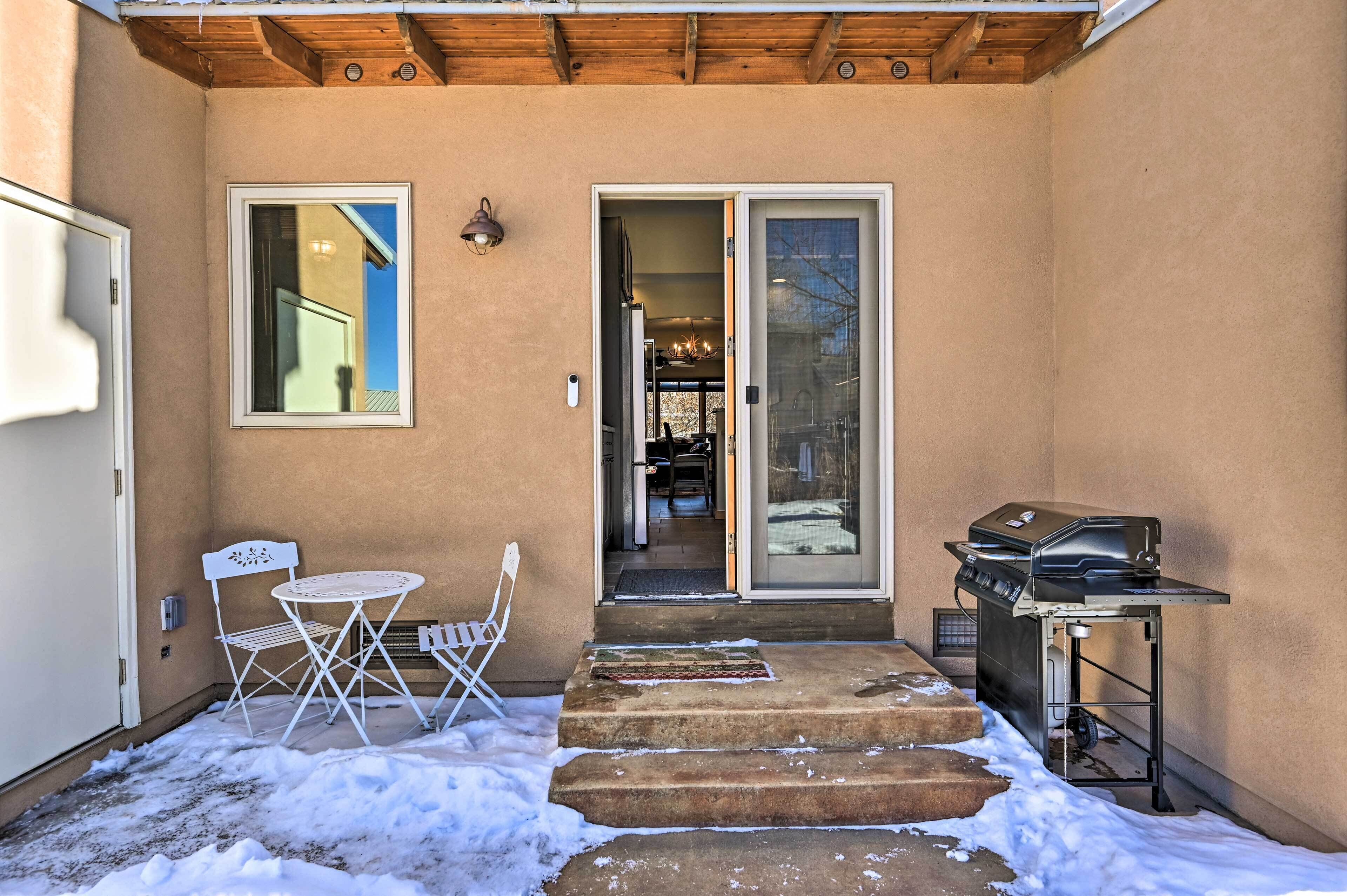 A covered patio with a grill, a folding table, and chairs.