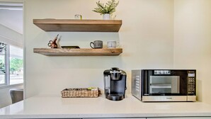Keittiössä on valkoiset kaapit, kahvinkeitin, mikroaaltouuni ja hylly, jossa on koriste-esineitä.