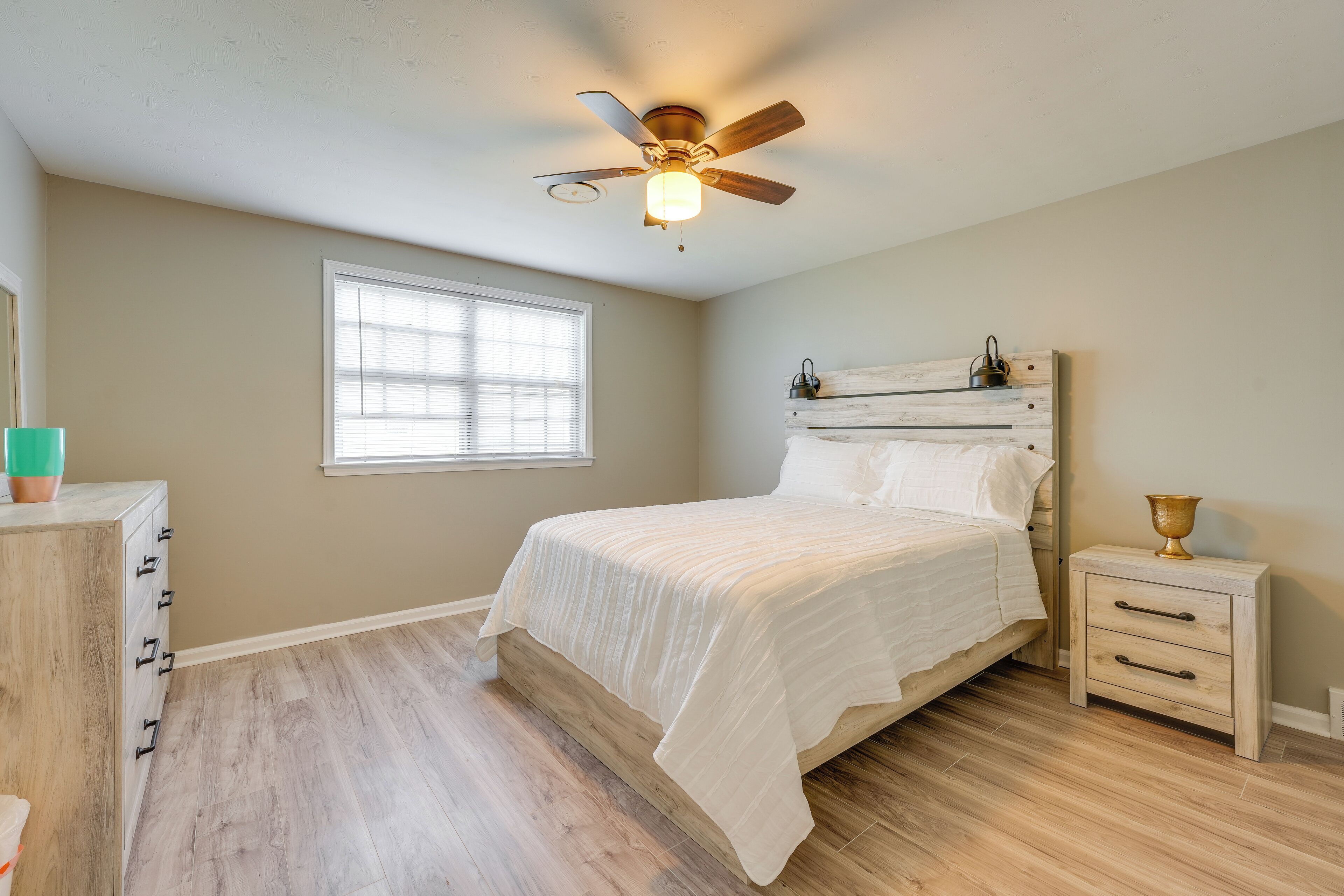A bedroom with a bed, a nightstand, a dresser, a ceiling fan, and a window.