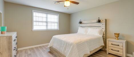 A bedroom with a bed, a nightstand, a dresser, a ceiling fan, and a window.