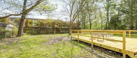 A wooden deck with outdoor furniture, surrounded by trees and a grassy yard.