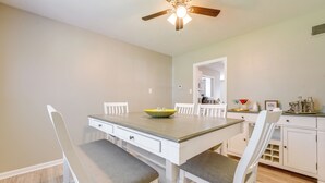 Un espace repas avec une table en bois, des chaises blanches et un ventilateur de plafond.