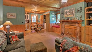 A cozy living room with a fireplace, wooden ceiling, and a dining area with chairs and a table. - Cozy Pine Mountain Cabin w/ Screened Porch & Yard! (Pine Mountain)