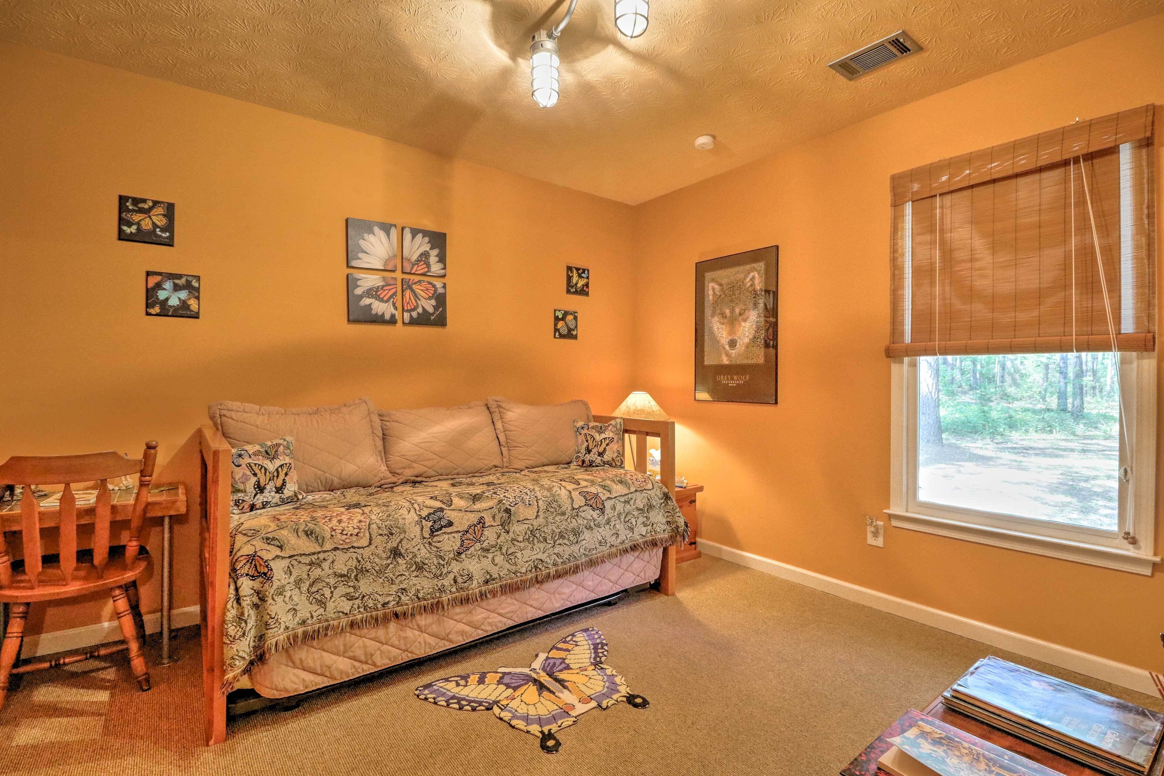 A cozy bedroom with a bed, a chair, a window with blinds, and wall art.