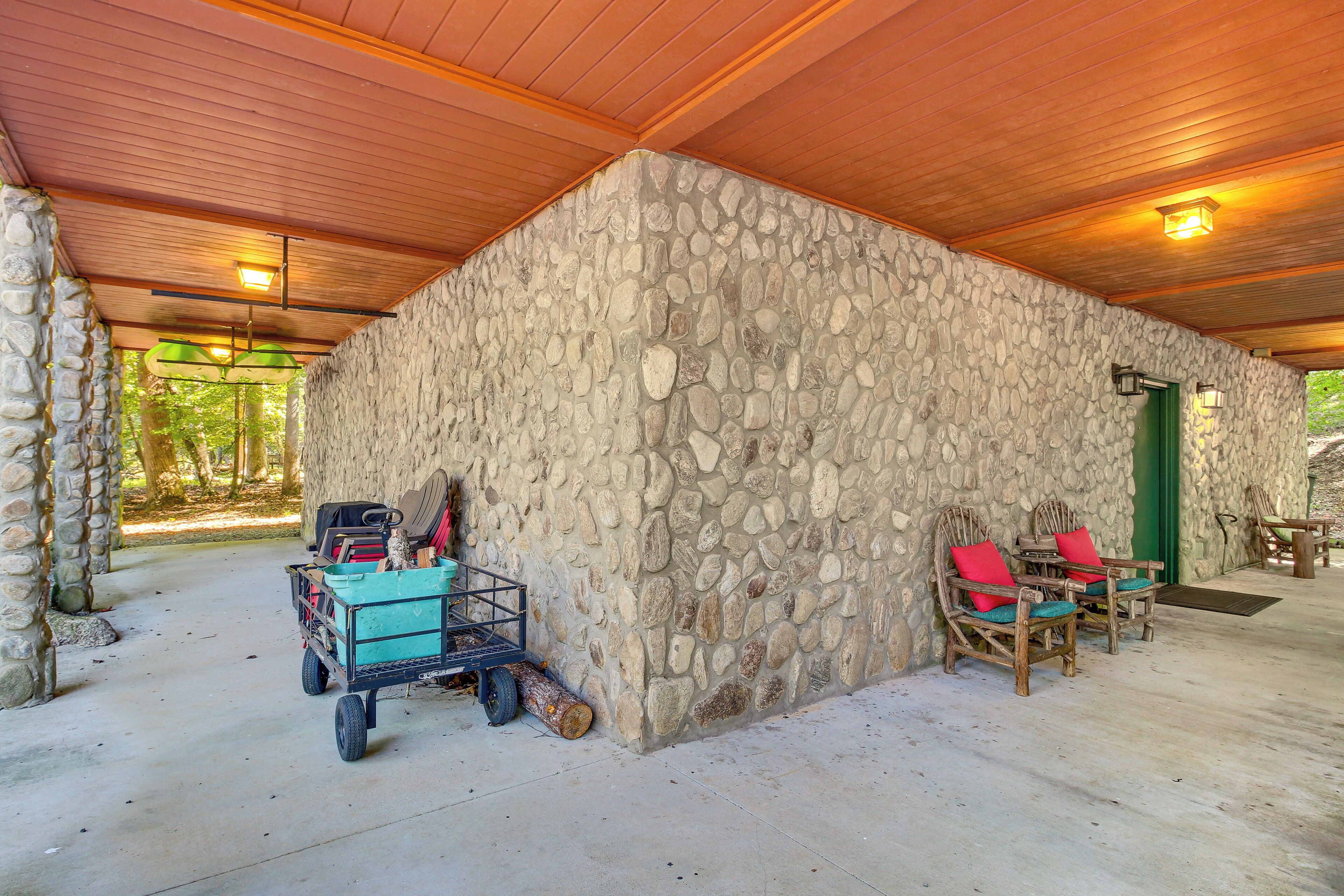 A stone-walled building with a wooden ceiling, a cart with items, and two wicker chairs with red cushions.