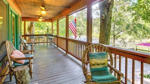 A wooden deck with chairs and a table, a flag, and a view of trees. - Serene Riverfront Escape in Ellijay, Georgia! (Ellijay)