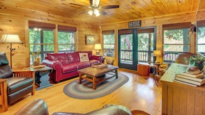 A cozy cabin interior with a wooden ceiling, leather furniture, and large windows offering a view of the outdoors. - Serene Riverfront Escape in Ellijay, Georgia! (Ellijay)