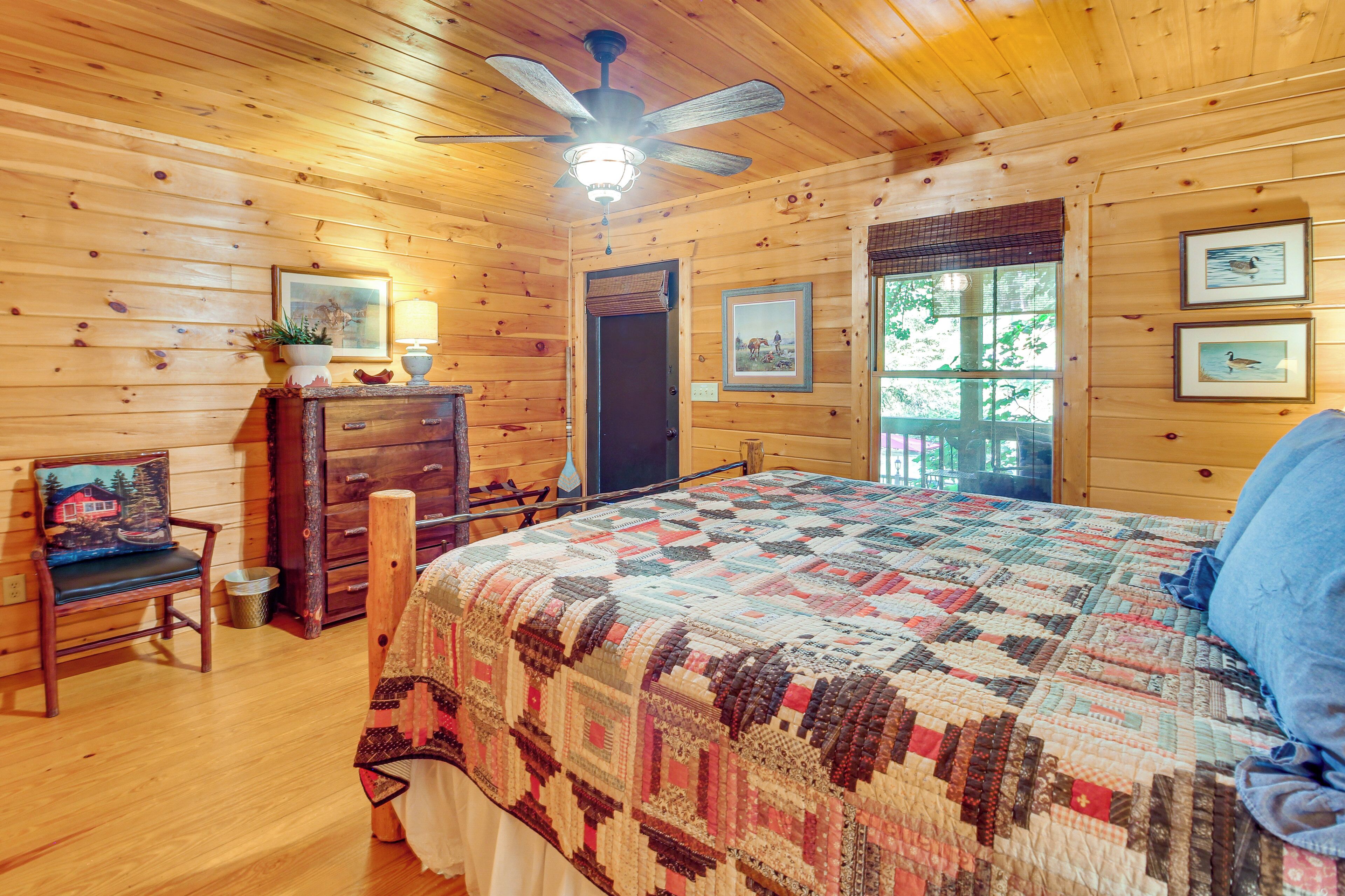 A cozy log cabin bedroom with a large bed, wooden walls, a ceiling fan, and framed pictures on the walls.