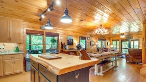 A spacious wooden cabin with a large kitchen area, dining table, and multiple windows offering views of the surrounding forest. - Serene Riverfront Escape in Ellijay, Georgia! (Ellijay)