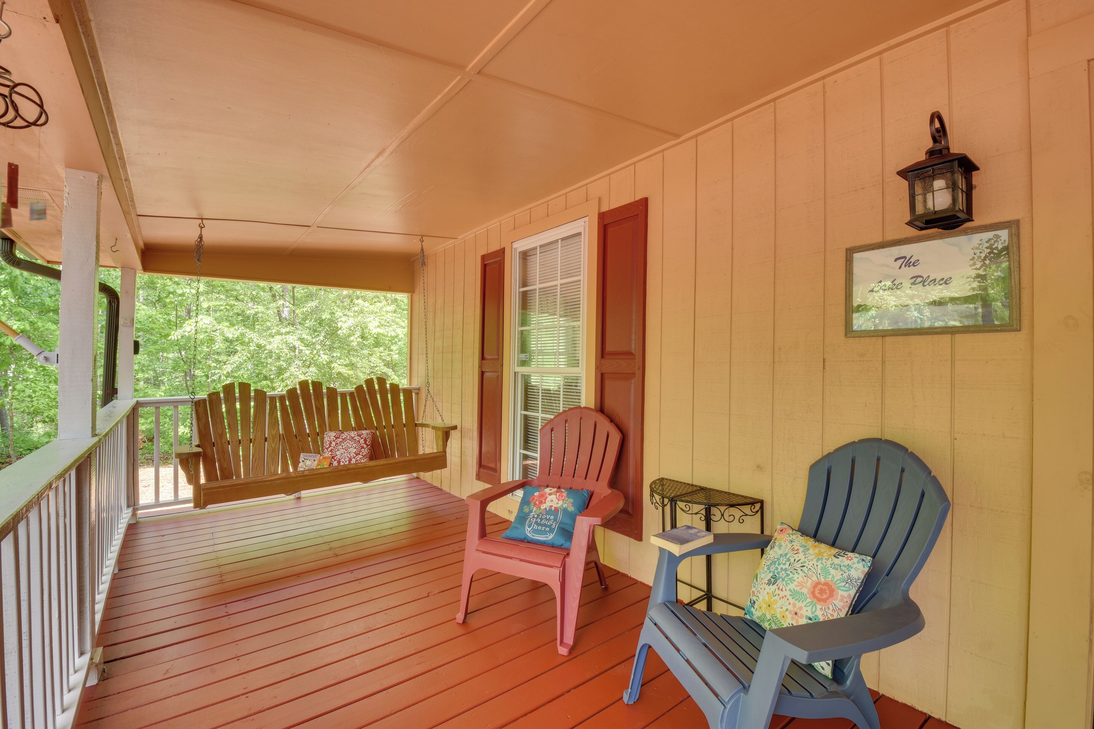 A wooden porch with a bench, two Adirondack chairs, and a small table with a lamp.