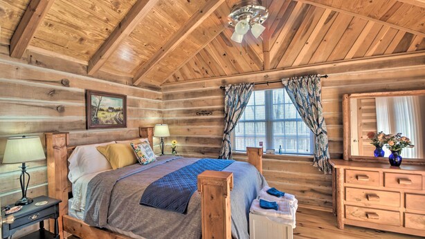 Un dormitorio de cabaña de troncos con una cama de madera, una mesita de noche, un aparador y un ventilador de techo.