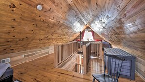 Interior de madera con techo inclinado, una escalera y vista a una habitación iluminada en rojo.