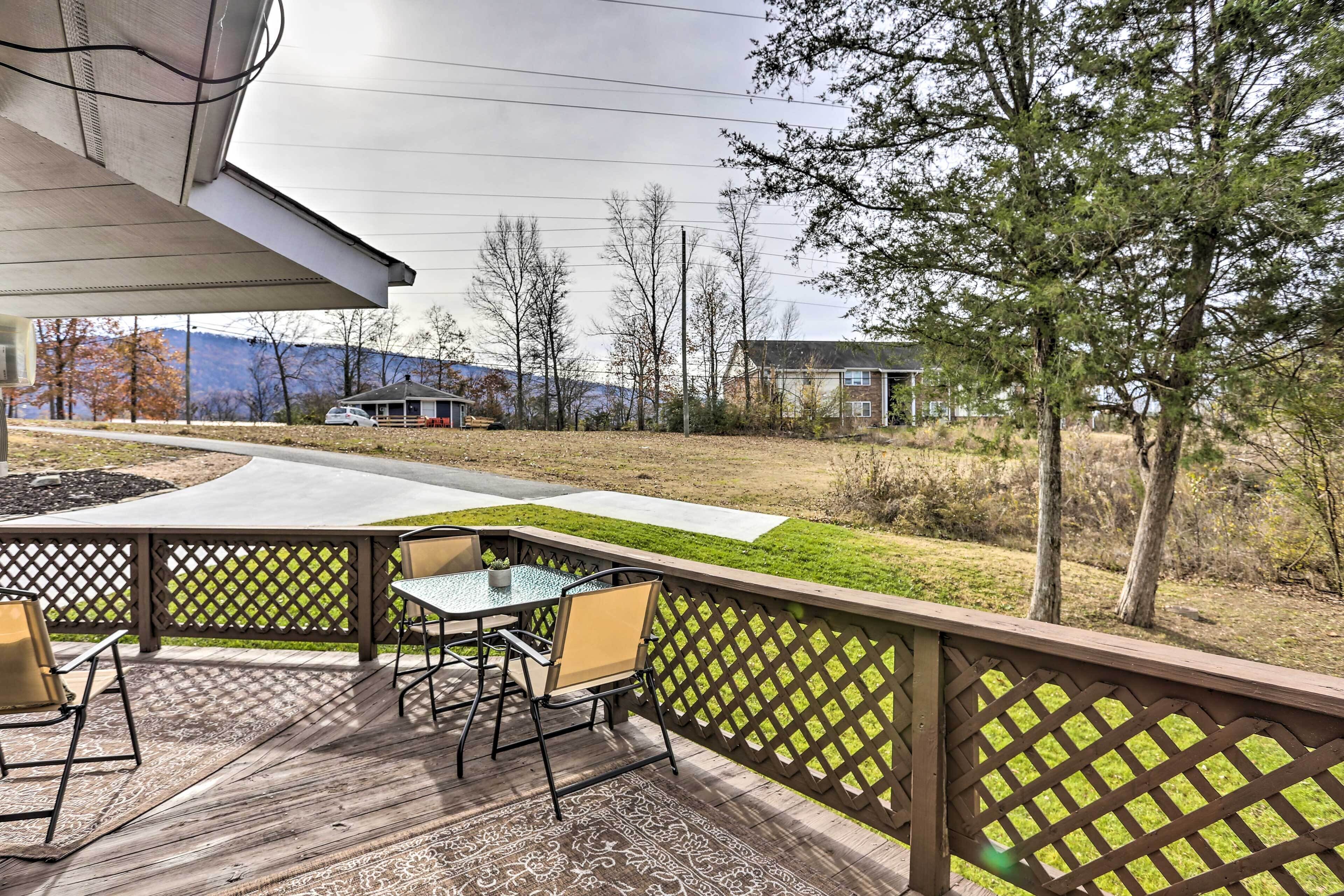 Une terrasse extérieure avec une table et des chaises, une plateforme en bois et une vue sur un espace verdoyant, avec des arbres et des bâtiments en arrière-plan.