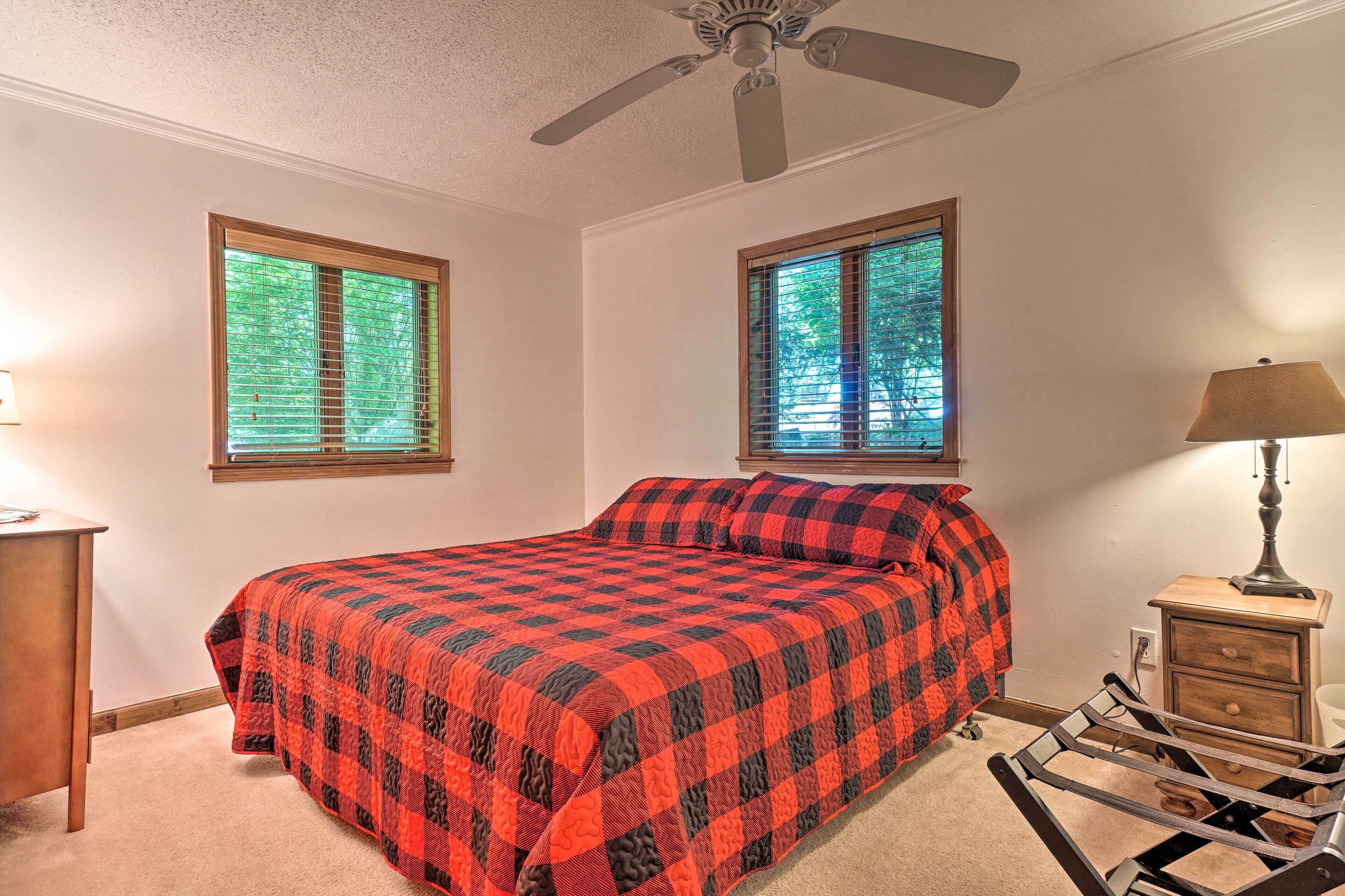 A bedroom with a bed, two windows, a ceiling fan, a nightstand, and a lamp.