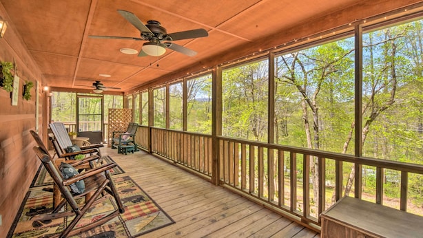 A covered porch with wooden flooring, ceiling fans, and large windows offering a view of trees. - Cozy Hiawassee Cabin w/ Fire Pit & Mtn Views! (Hiawassee)