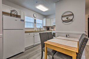 A compact kitchen with white cabinets, a refrigerator, a dining table with chairs, and a wall-mounted clock. - Downtown Ocean Springs Duplex w/ AC 1 Mi to Beach (Ocean Springs)